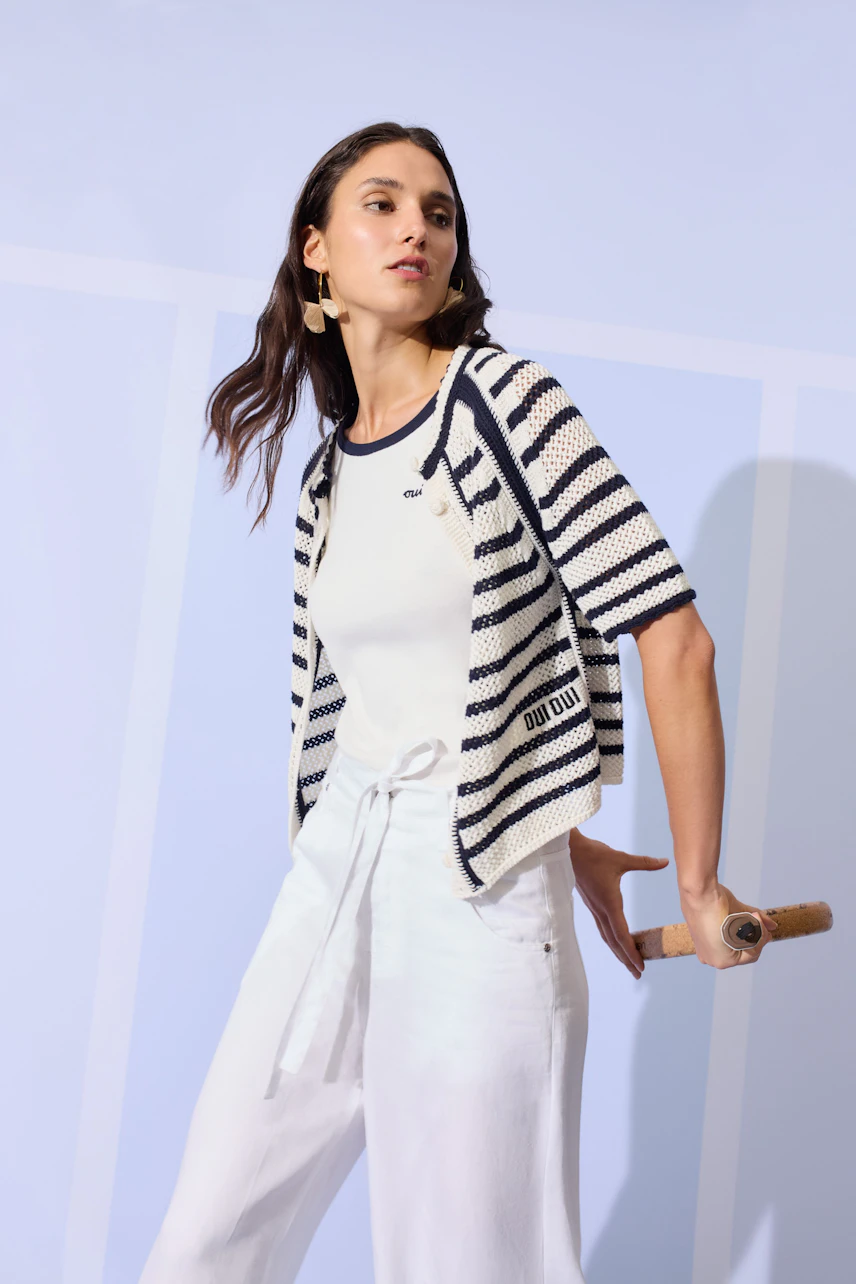 Casual striped cardigan: Woman in navy and white striped cardigan over a white top, holding a wooden handle.