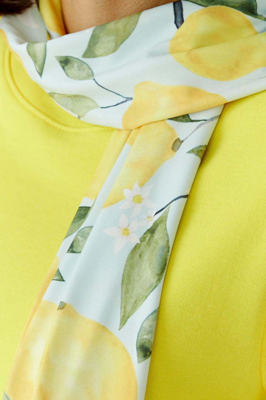 Bright scarf with lemon print on a woman in a yellow top, adding a fresh touch to her outfit.