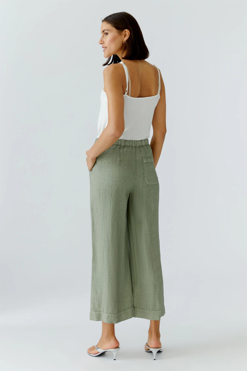 Lässige Damen-Hose: Frau in grüner, weiter Hose und weißem Top, seitlich stehend, mit entspanntem Ausdruck.