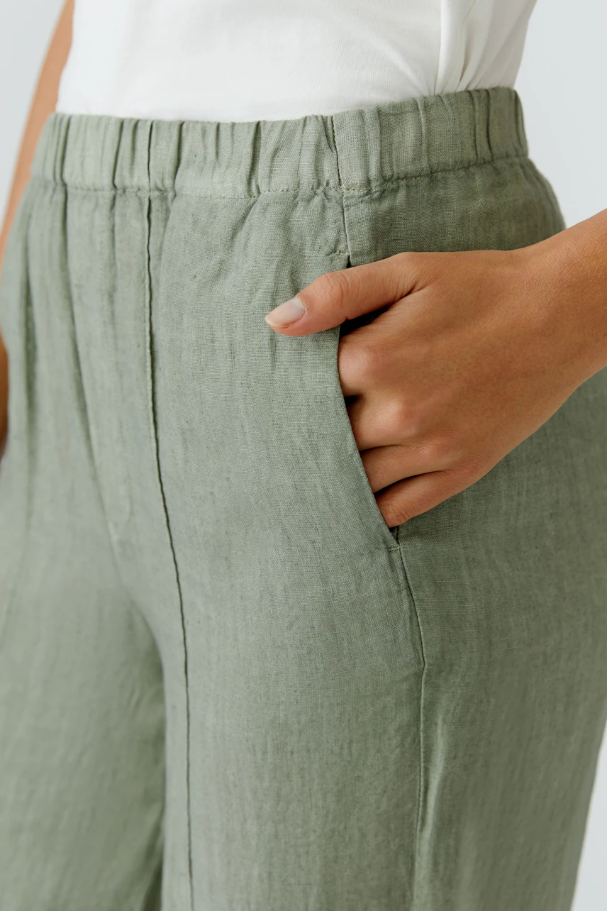 Lässige Damen-Hose: Frau in grüner Leinenhose mit elastischem Bund und seitlichen Taschen.