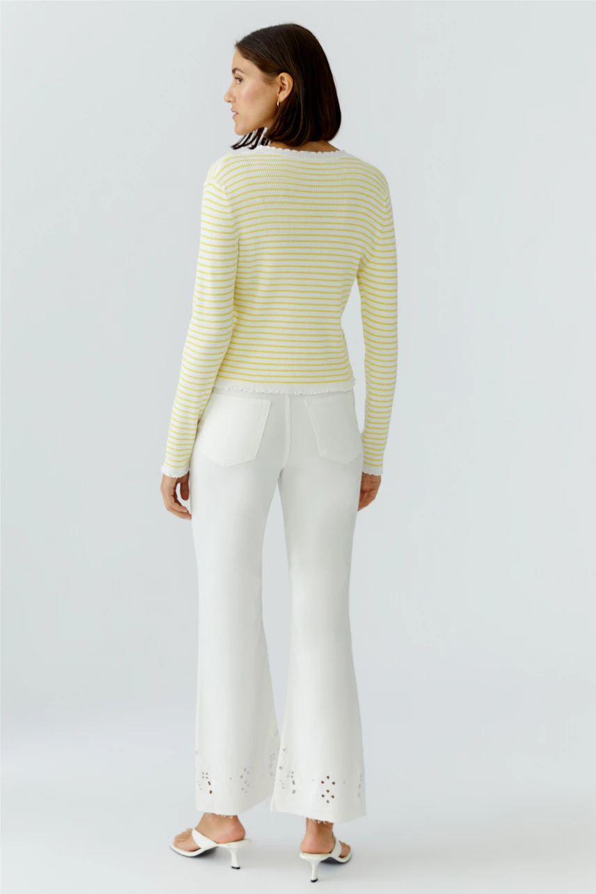 Frau in gestreifter Strickjacke: Gelb-weiße Streifen, kombiniert mit weißer Hose, lässiger Look.
