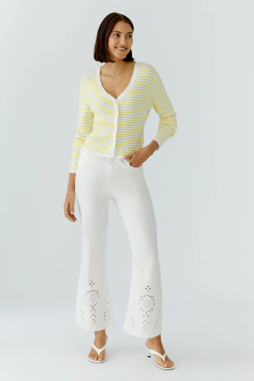 Strickjacke: Frau in gelb-weiß gestreifter Strickjacke und weißer Hose, von hinten gesehen.