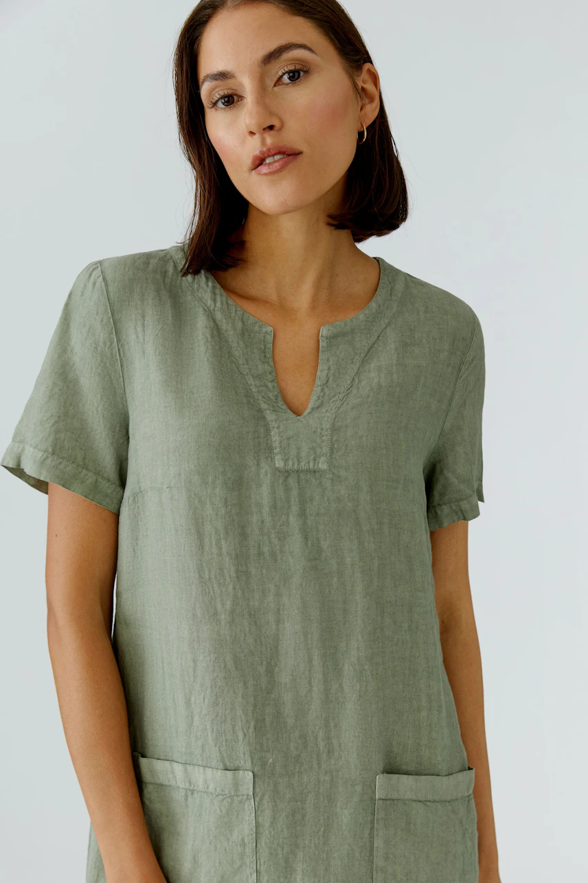 A-Linien-Kleid: Frau in grünem Leinenkleid mit kurzen Ärmeln und V-Ausschnitt, lässig und modern.