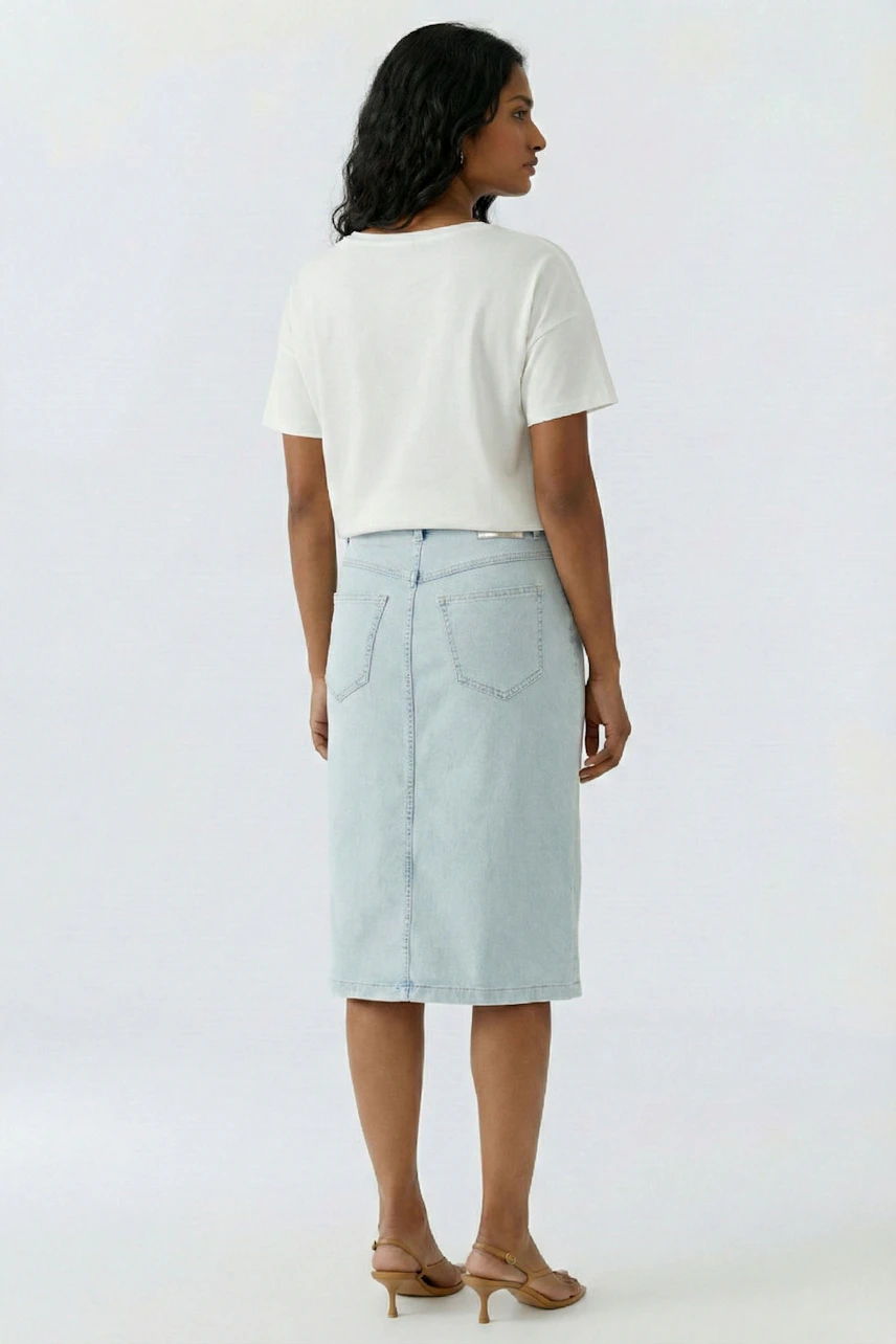 Casual denim skirt: Woman in light blue jeans skirt and white tee, standing with relaxed posture.