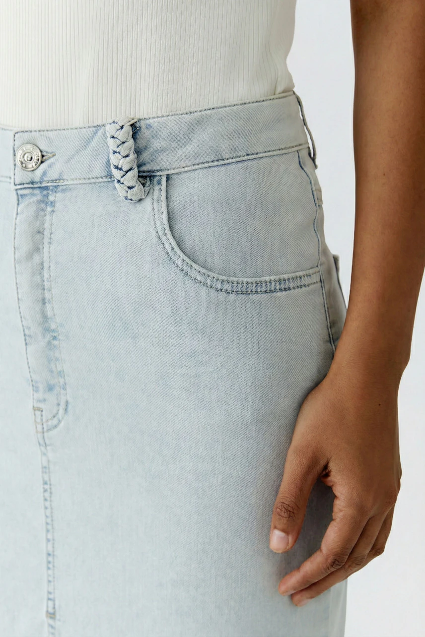 Casual denim skirt: Woman in light blue jeans skirt with braided belt detail, wearing a white top.