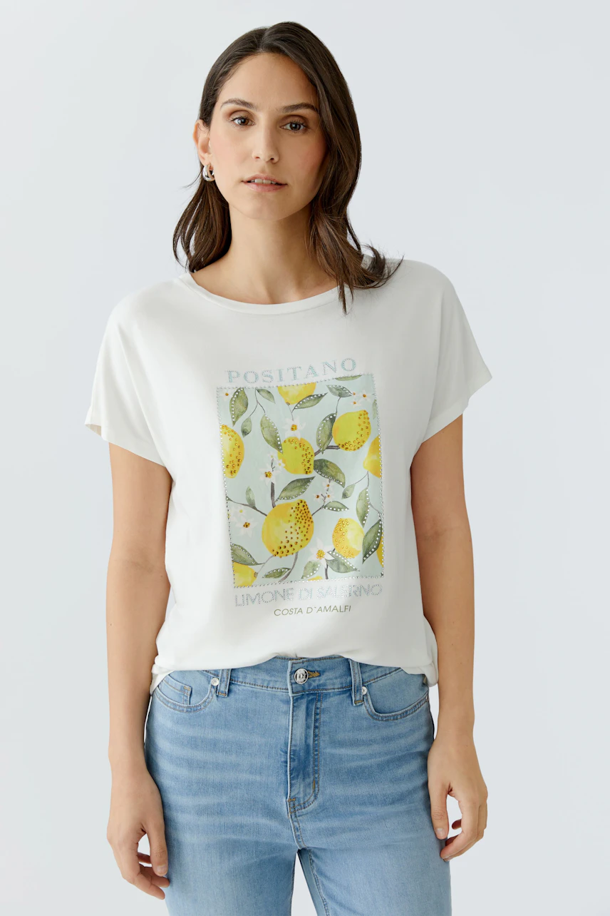 Damen-T-Shirt: Frau im weißen T-Shirt mit Zitronenprint und blauer Jeans, lässig und modern.