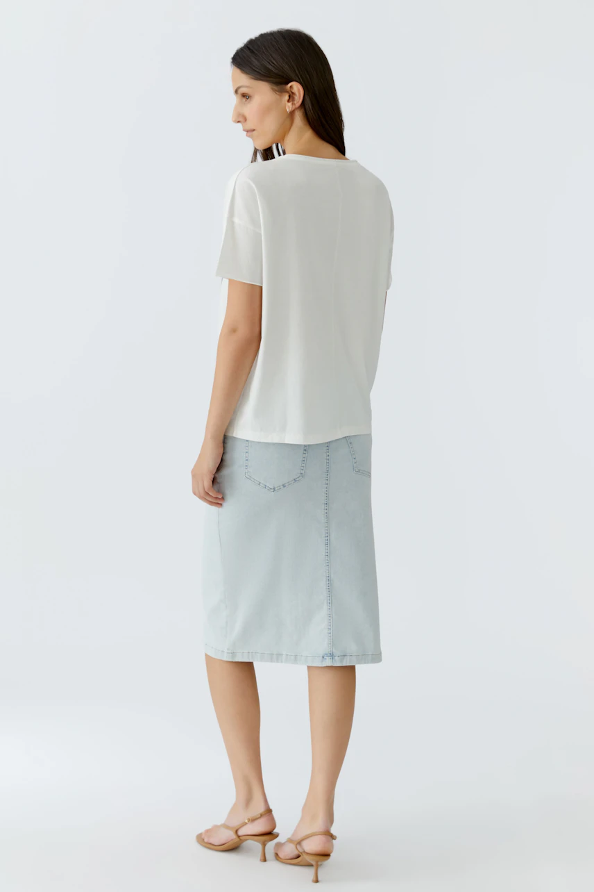 Damen-T-Shirt: Frau in weißem T-Shirt und ausgestellten Hosen mit Lochmuster von hinten.