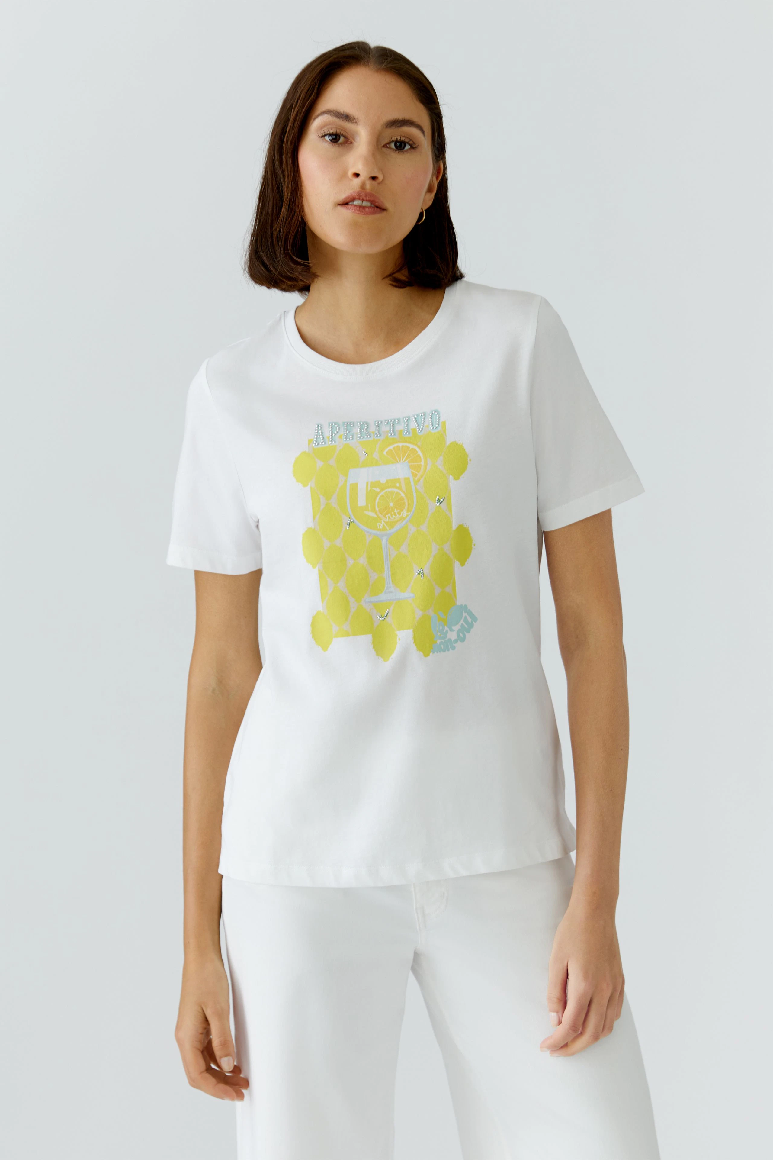 Casual women's T-shirt: Woman in white T-shirt with yellow graphic, paired with white pants, looks relaxed.