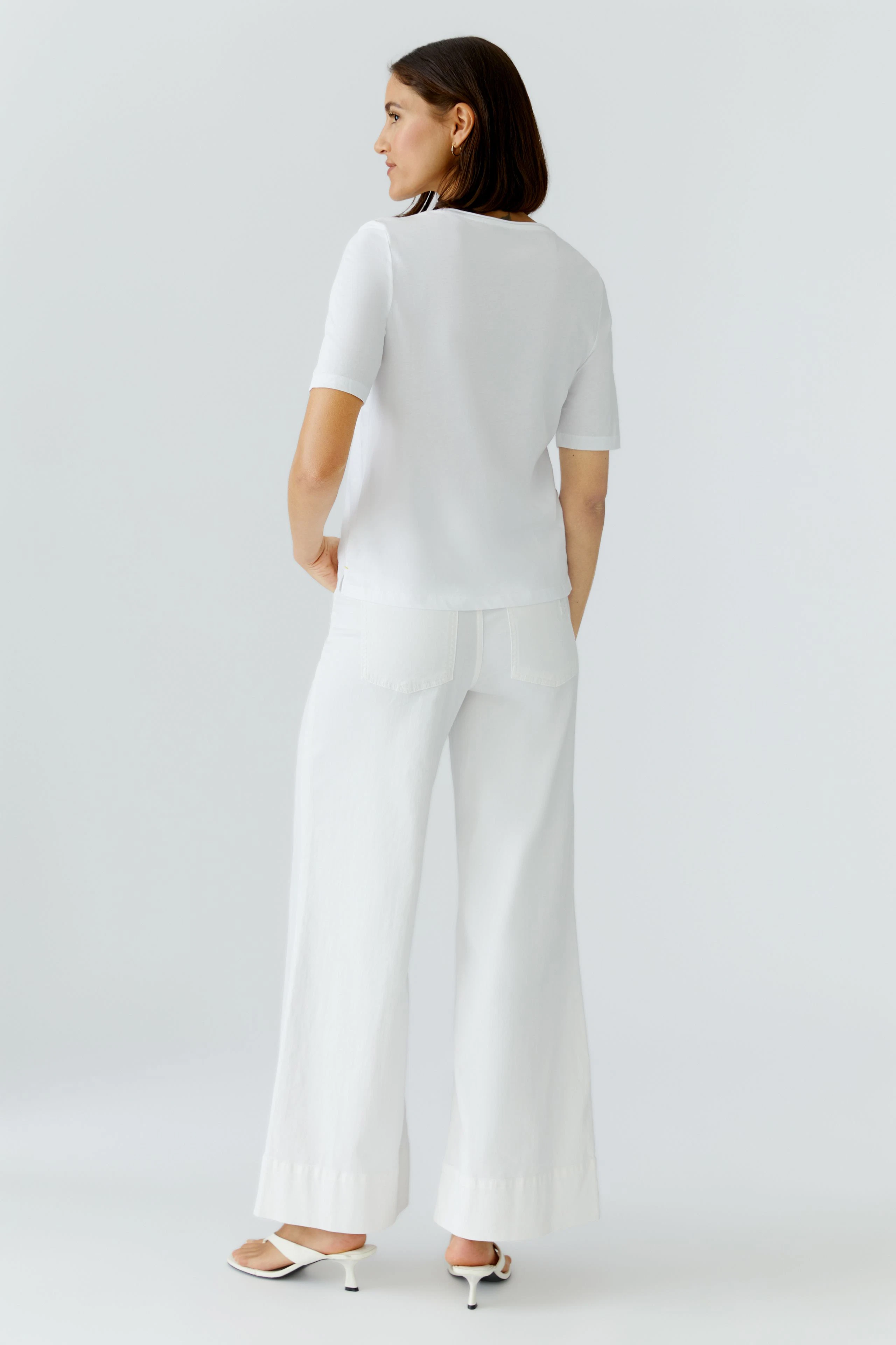 Casual women's T-shirt: Woman in a white T-shirt and wide-leg pants, viewed from the back.