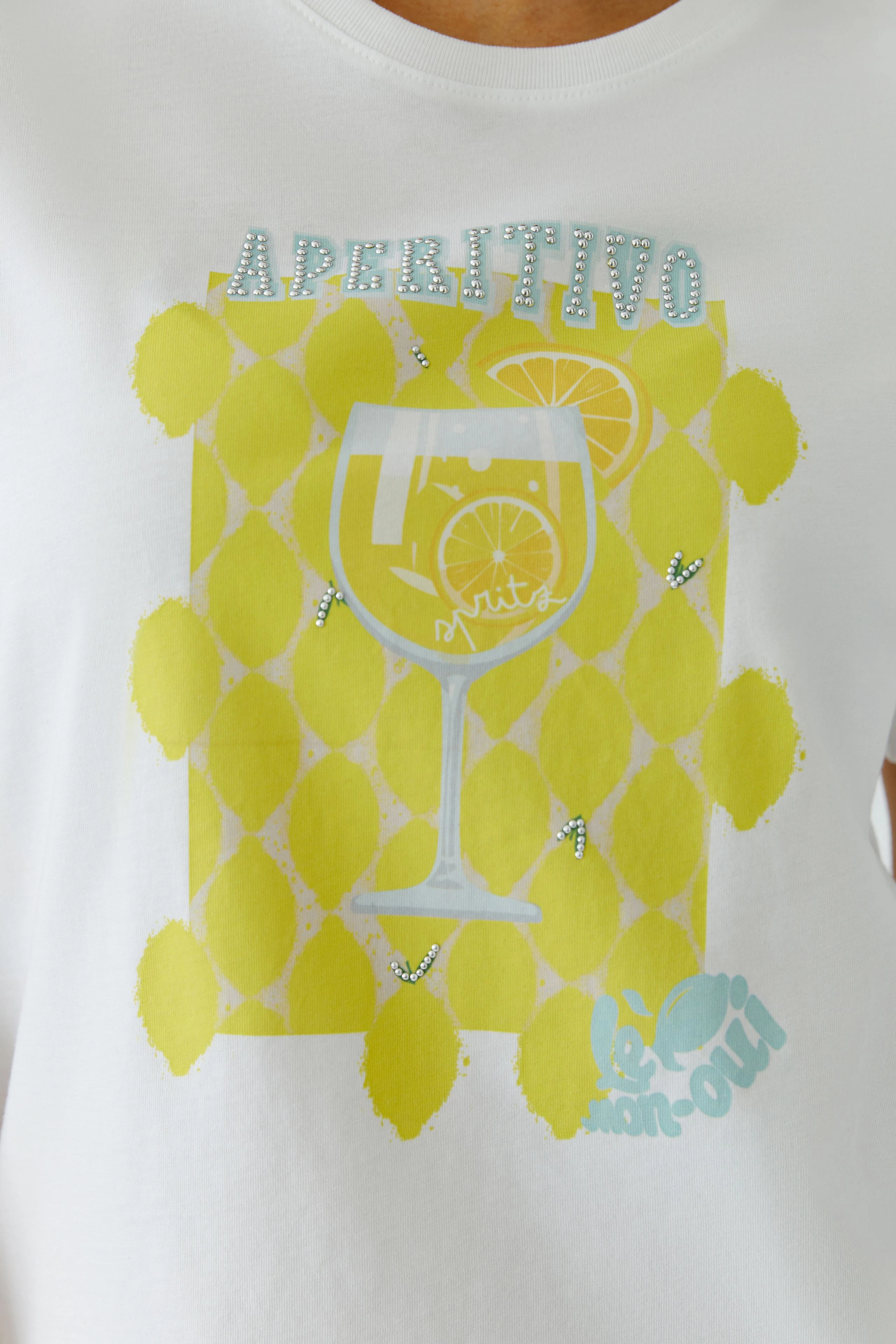 White T-shirt with lemon print and "Aperitivo" text, worn by a woman. Casual and vibrant design.