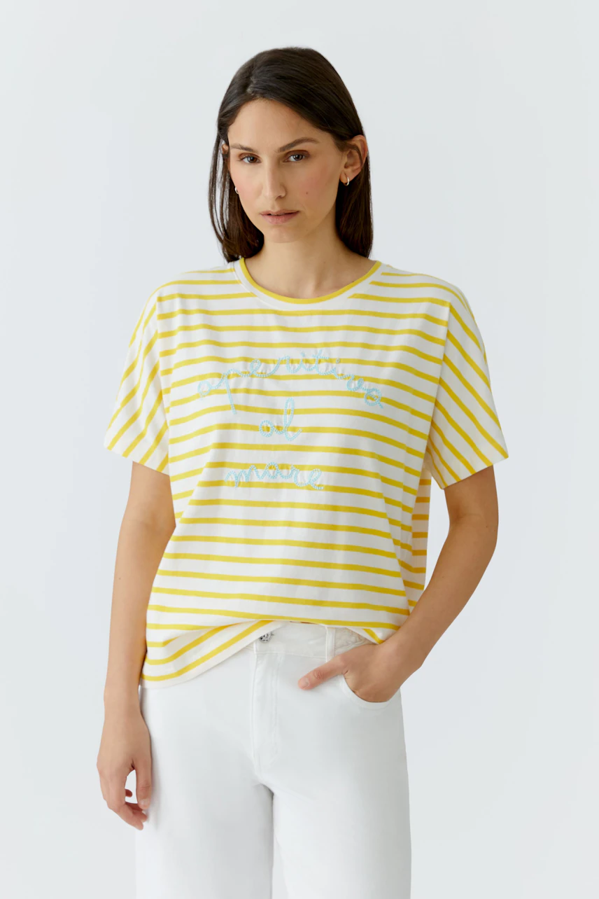 Lässiges Damen-T-Shirt: Frau im gelb-weiß gestreiften T-Shirt mit Schriftzug, kombiniert mit weißen Hosen.