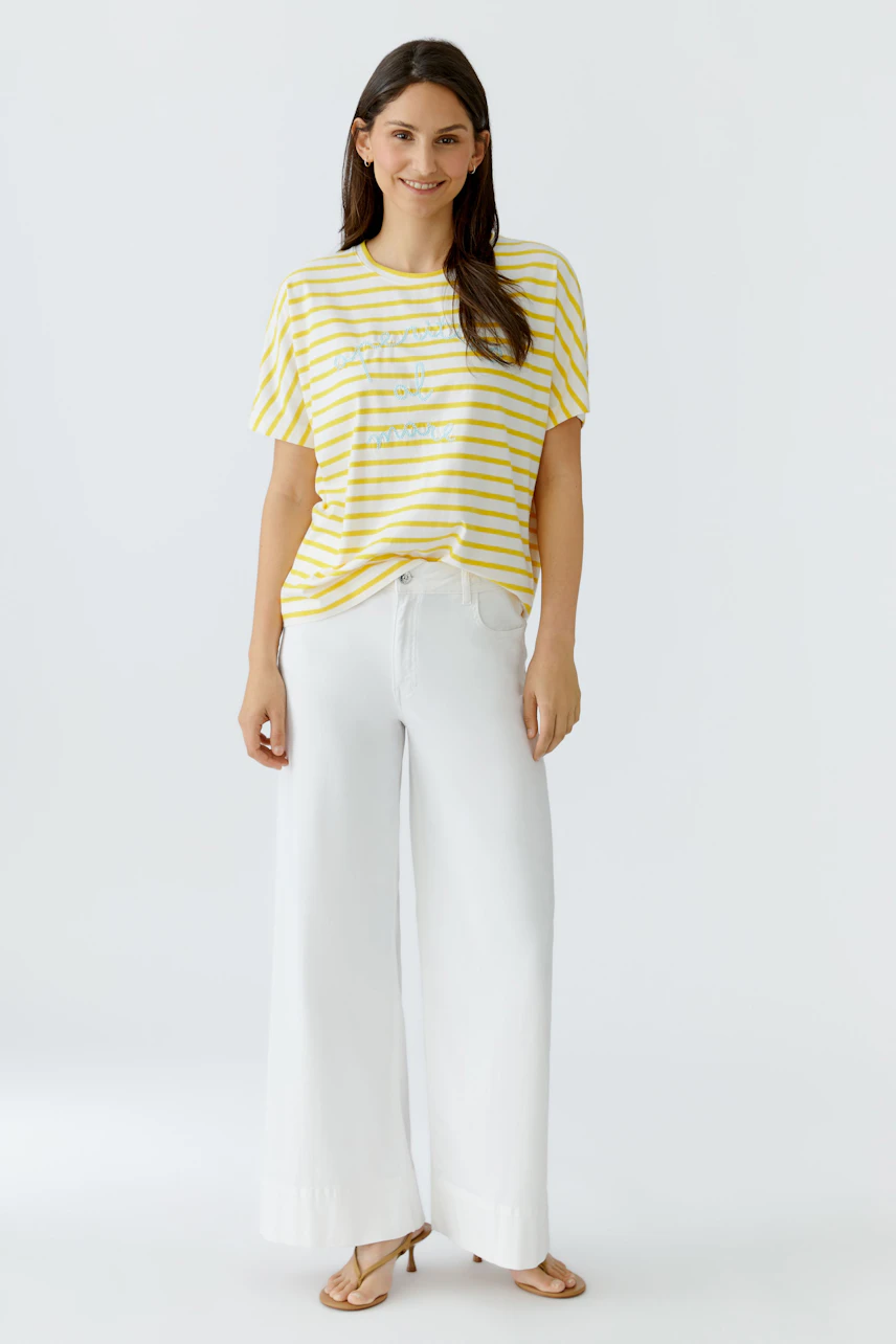 Damen-T-Shirt: Frau im gelb-weiß gestreiften T-Shirt und weißen Hosen, lässig und modern.