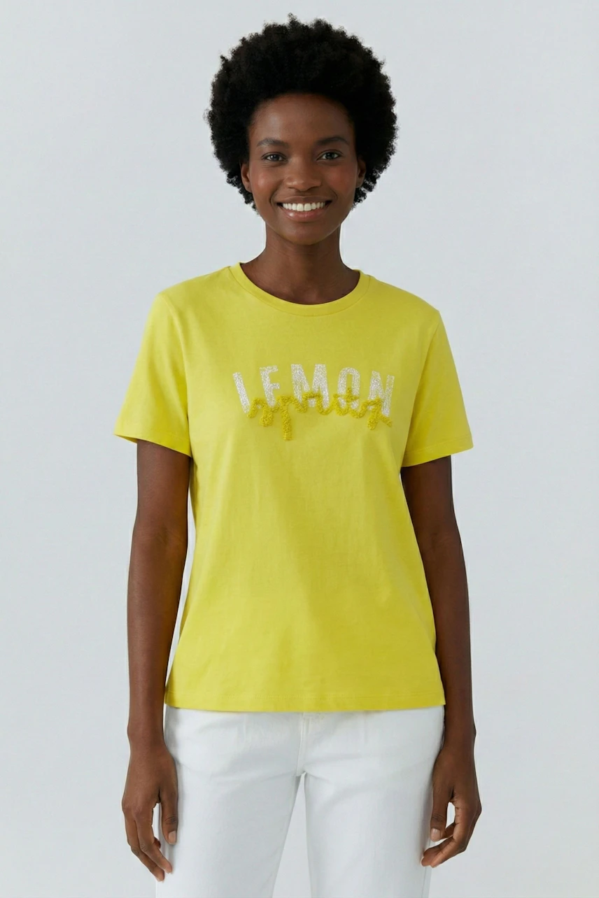 Casual women's T-shirt: Smiling woman in a yellow T-shirt with 'LEMON' print, paired with white pants.