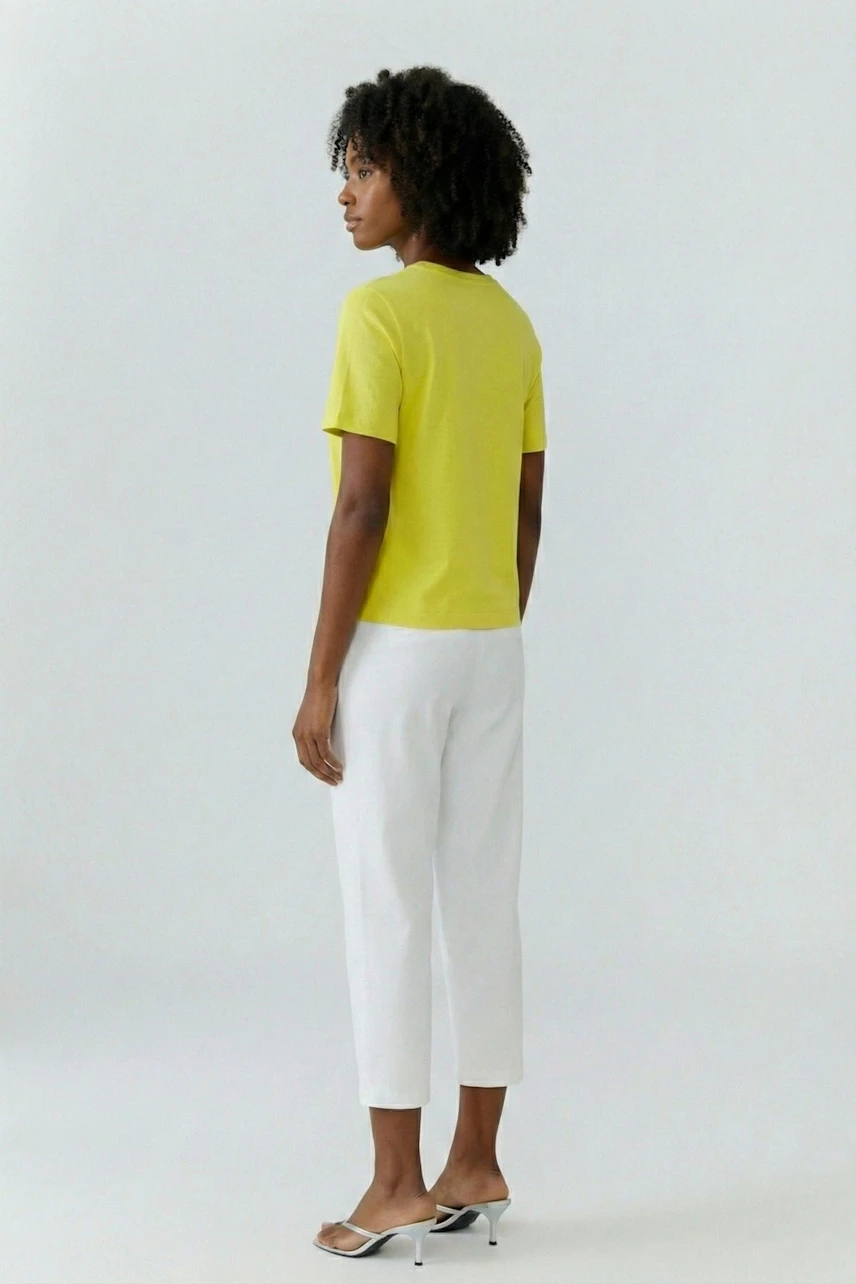 Casual T-shirt: Woman in a bright yellow T-shirt and white pants, standing confidently.