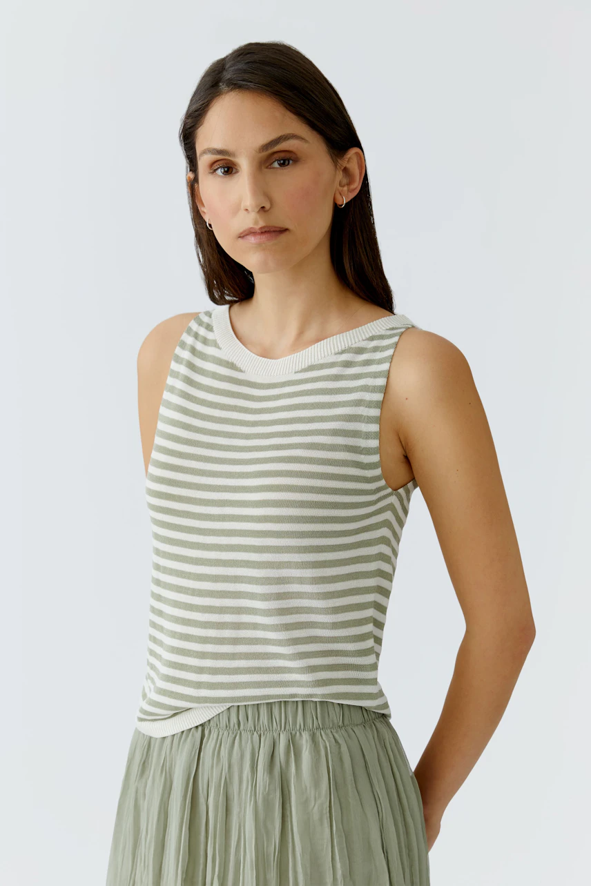 Gestreiftes Damen-Top: Frau im ärmellosen, grün-weiß gestreiften Top mit lockerem Rock schaut ernst.
