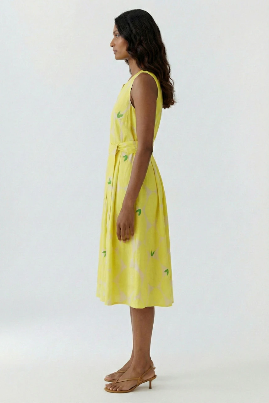 Frau im gelben Midikleid mit grünem Muster, seitlich stehend. Sommerlich und leicht, ideal für warme Tage.