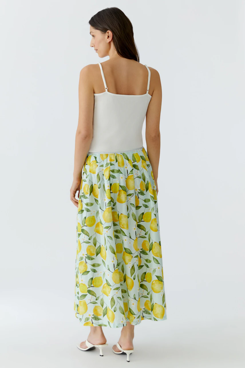 Faltenrock mit Zitronenmuster: Frau im weißen Top und langem, gemustertem Rock von hinten.