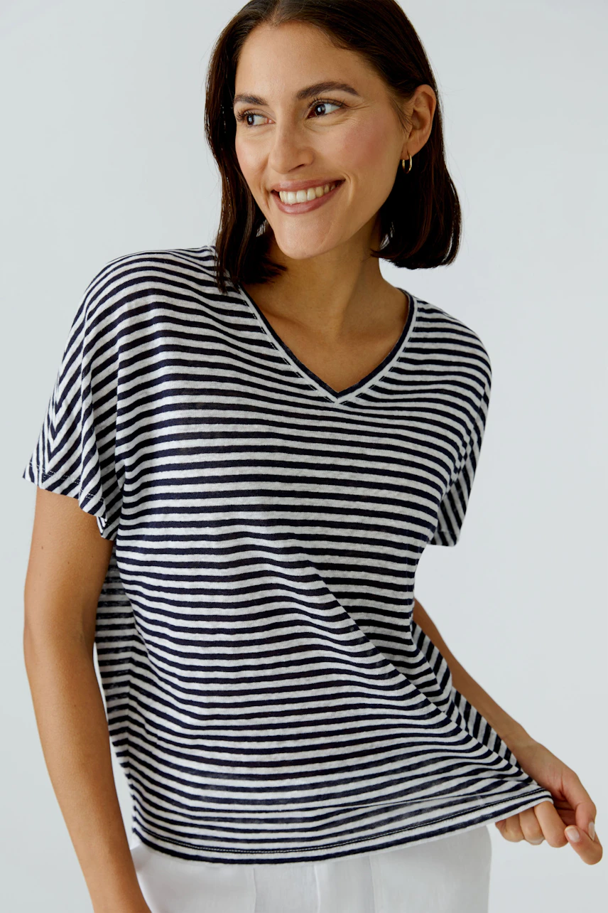 Casual women's T-shirt: Smiling woman in a striped V-neck T-shirt, short sleeves, and white pants.