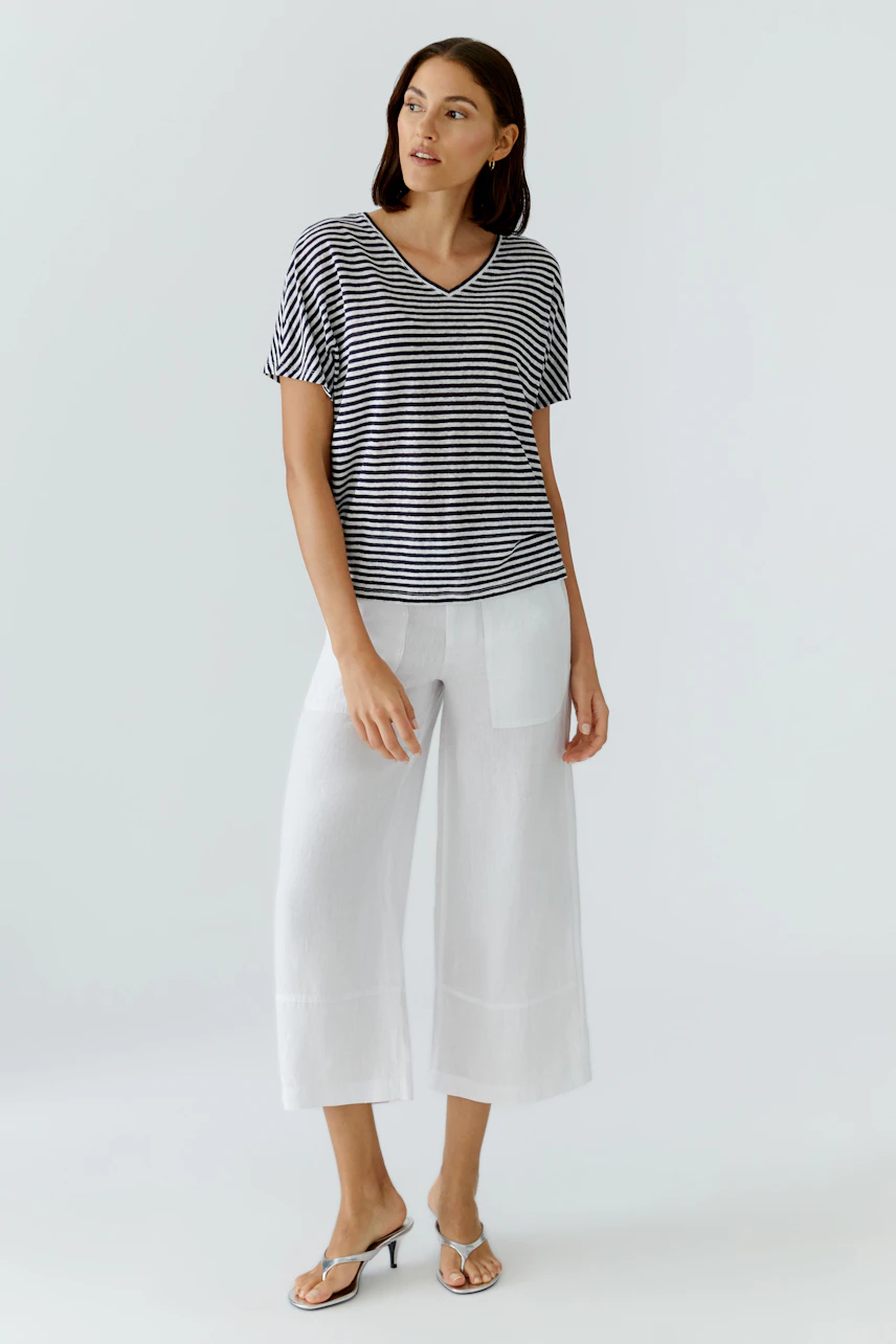 Casual women's T-shirt: Woman in striped T-shirt and white pants, standing confidently.