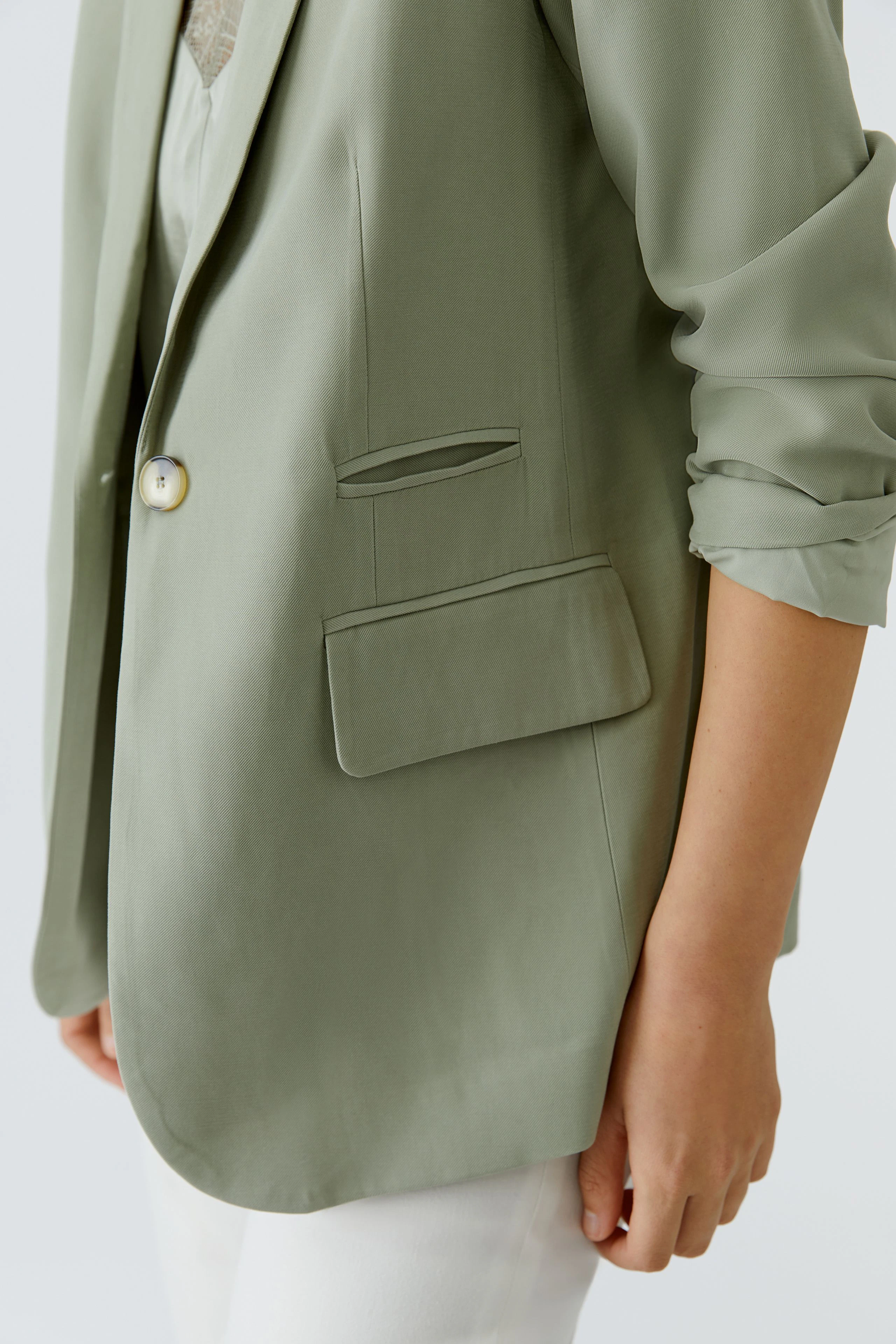 Casual women's blazer: Woman in a light green blazer with rolled sleeves and white pants.