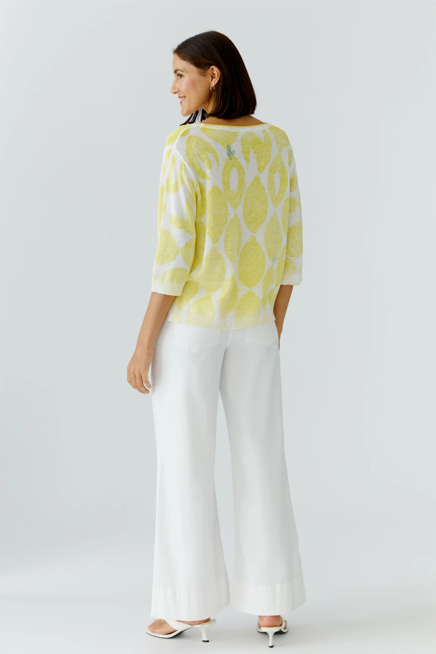 Frau im gelben Pullover mit weißem Muster, kombiniert mit weißen Hosen. Lässiger Look für den Alltag.