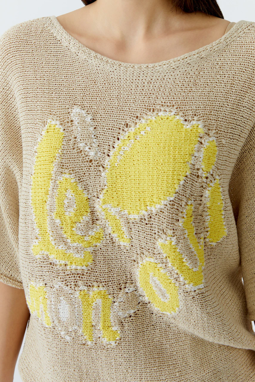 Lässiger Damen-Pullover: Frau im beigen Strickpullover mit gelbem Print und weitem Ausschnitt.