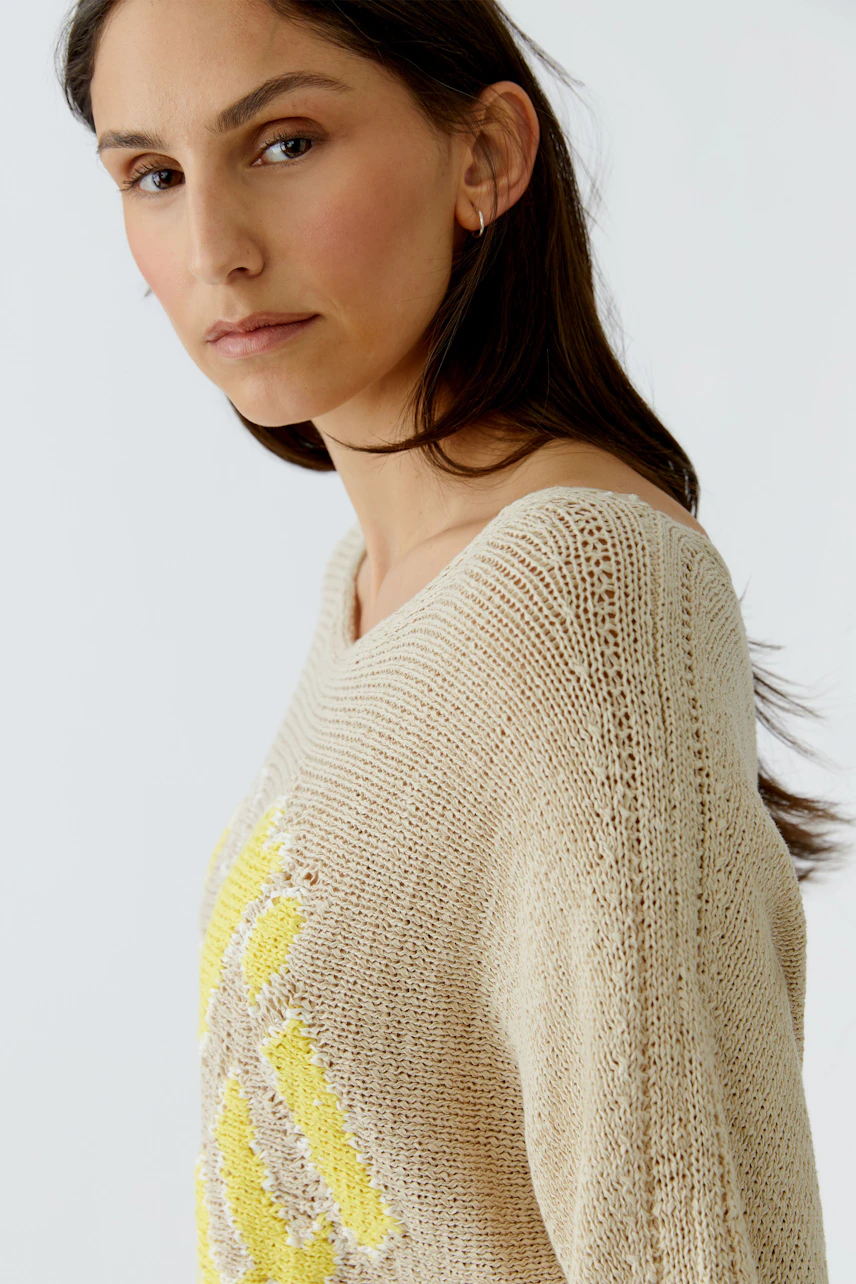 Damen-Pullover: Frau im beigen Strickpullover mit gelbem Muster, seitlich blickend.