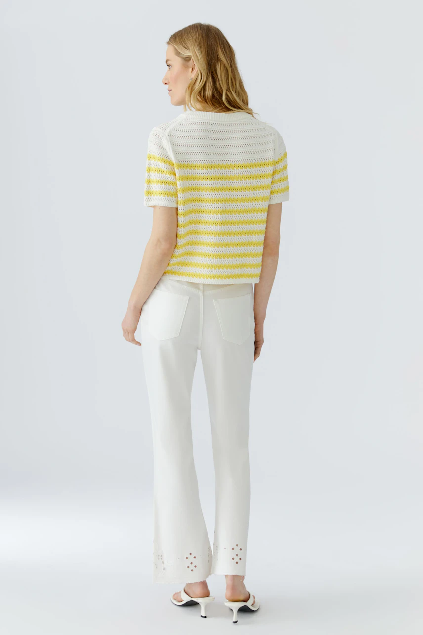 Frau im gestreiften Pullover in Gelb-Weiß, kombiniert mit weißer Hose. Rückansicht.