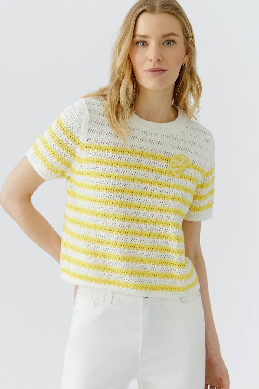 Damen-Pullover: Frau im gestreiften, gelb-weißen Pullover aus Häkelstoff, kombiniert mit weißen Hosen.