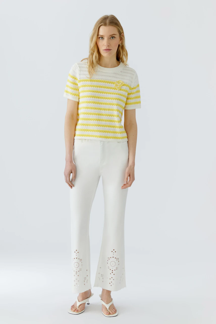 Frau im gestreiften Pullover: Gelb-weiß gestreifter Pullover, kombiniert mit weißer Hose und Sandalen.