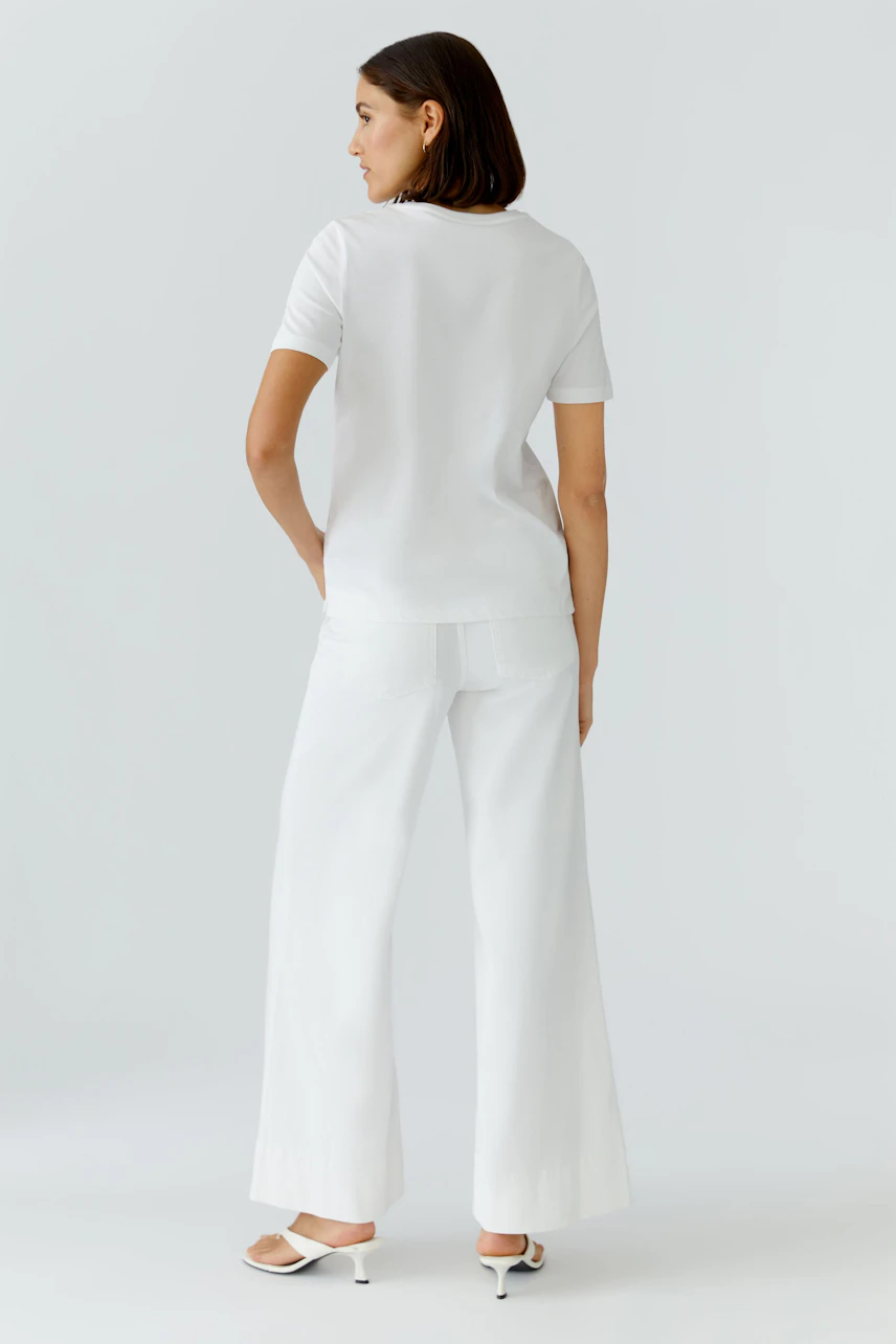 Weißes Damen-T-Shirt: Frau im schlichten T-Shirt und weiter Hose, von hinten gesehen.