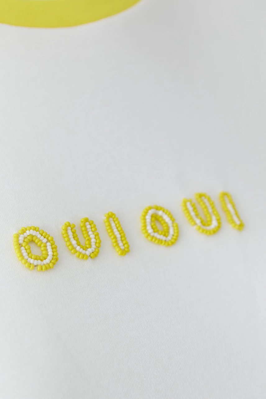 Weißes Damen-T-Shirt: Frau trägt ein schlichtes T-Shirt mit gelbem Kragen und "Oui Oui" Schriftzug.