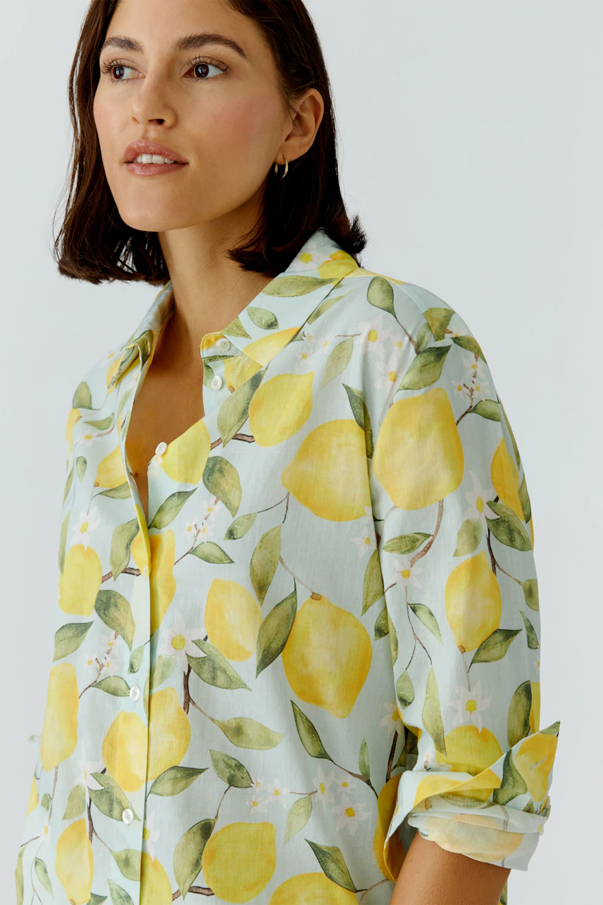 Hemdbluse mit Zitronenmuster: Frau trägt eine farbenfrohe Bluse mit gelben Zitronen und grünen Blättern.