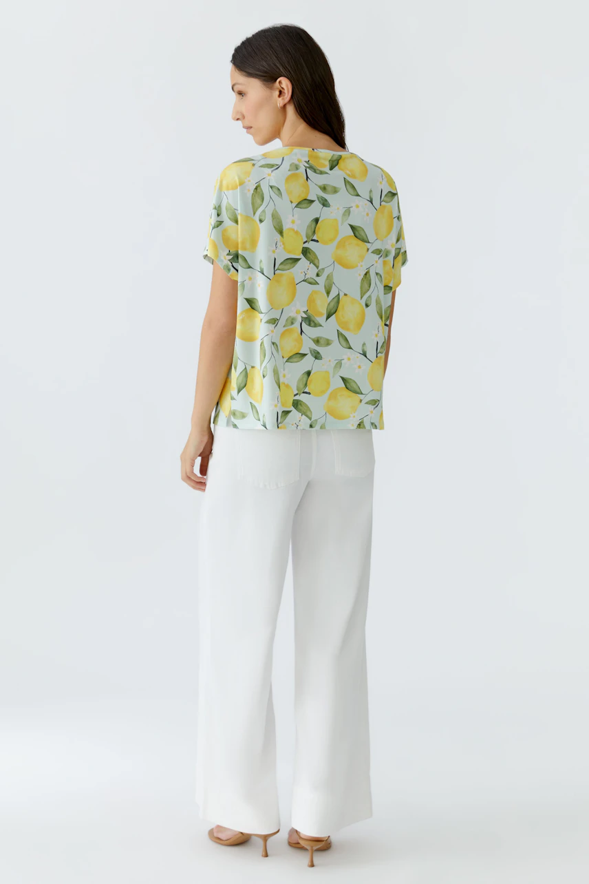 Damen-T-Shirt: Frau im locker fallenden T-Shirt mit Zitronenprint und weißen Hosen von hinten.