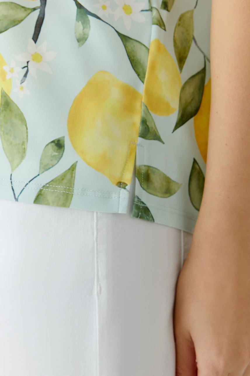 Damen-T-Shirt: Frau trägt ein T-Shirt mit Zitronenprint und weißen Hosen, sommerlich und frisch.