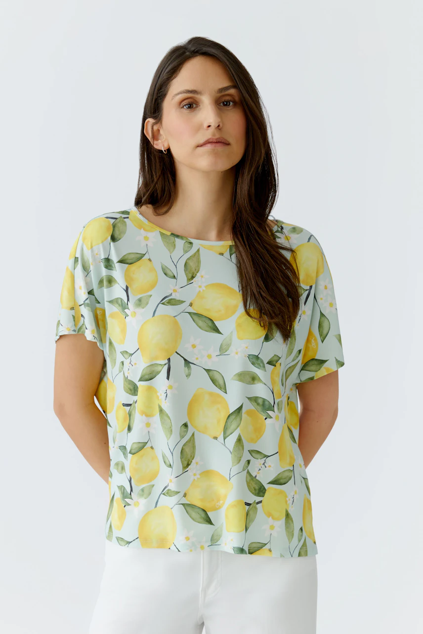Damen-T-Shirt: Frau im hellen T-Shirt mit Zitronenmuster und weißen Hosen, lässig und frisch.