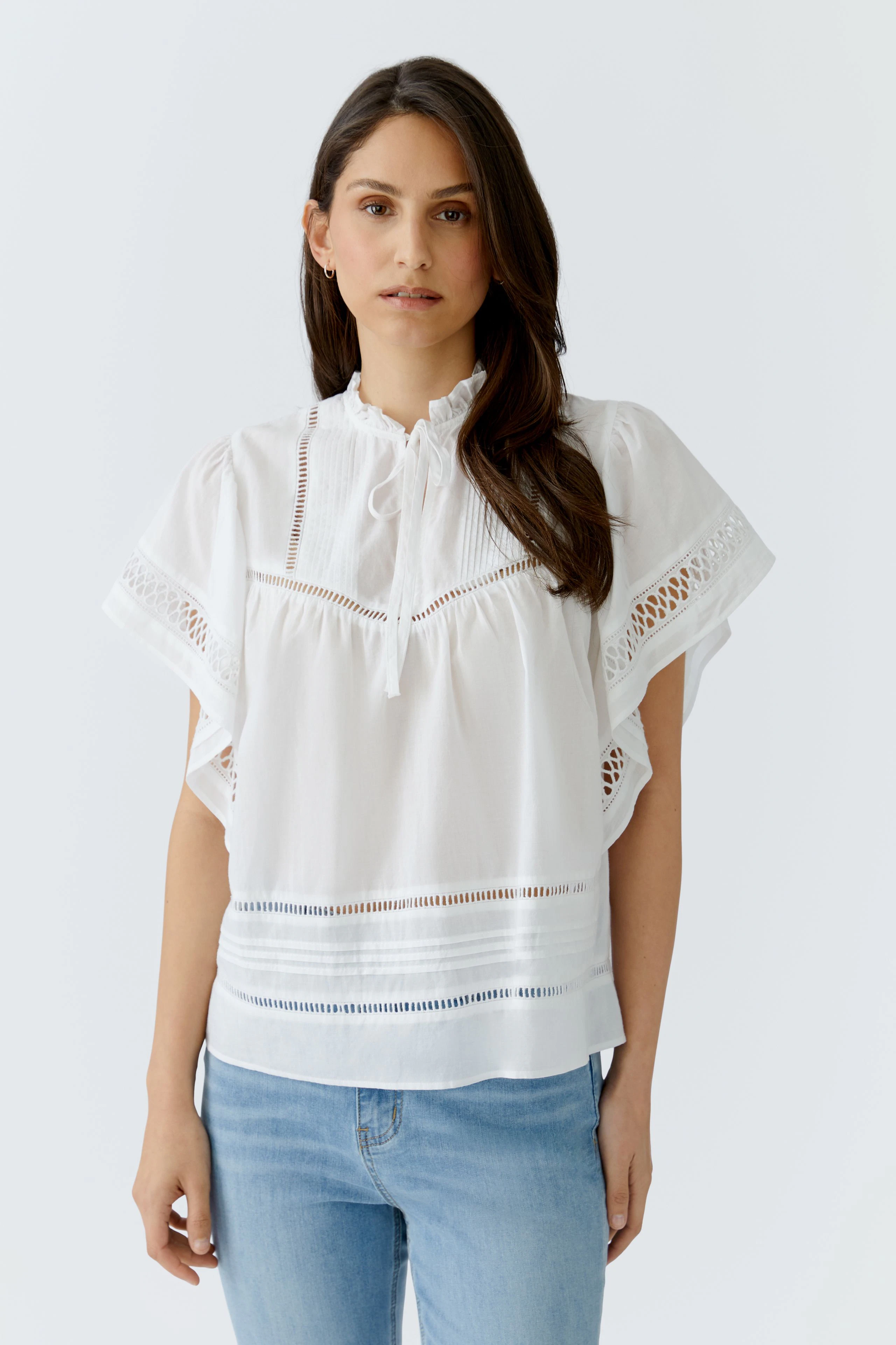 Casual women's blouse: Woman in a white blouse with lace details and light blue jeans, looking relaxed.