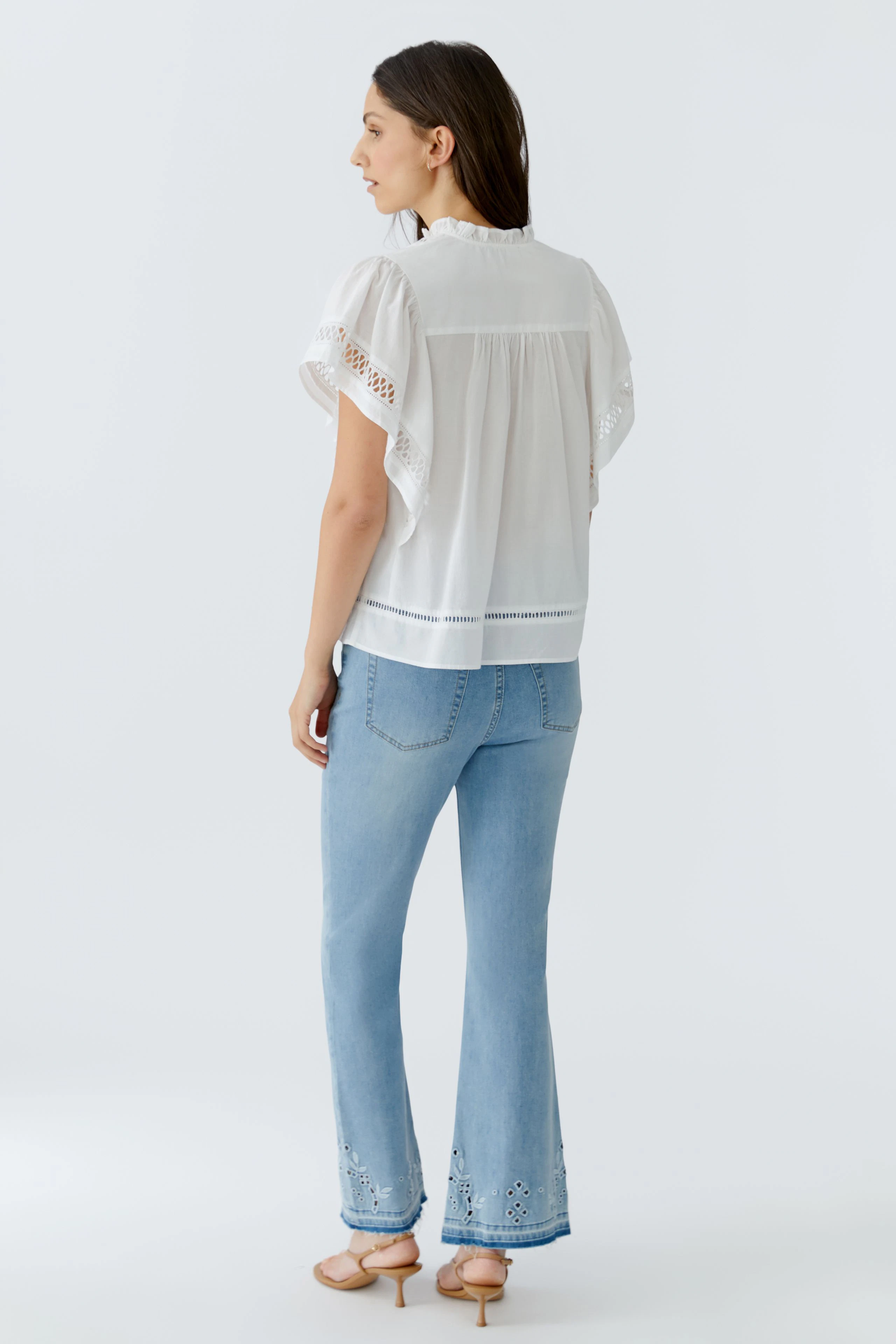 Casual blouse: Woman in a white blouse with lace sleeves and light blue jeans, standing confidently.