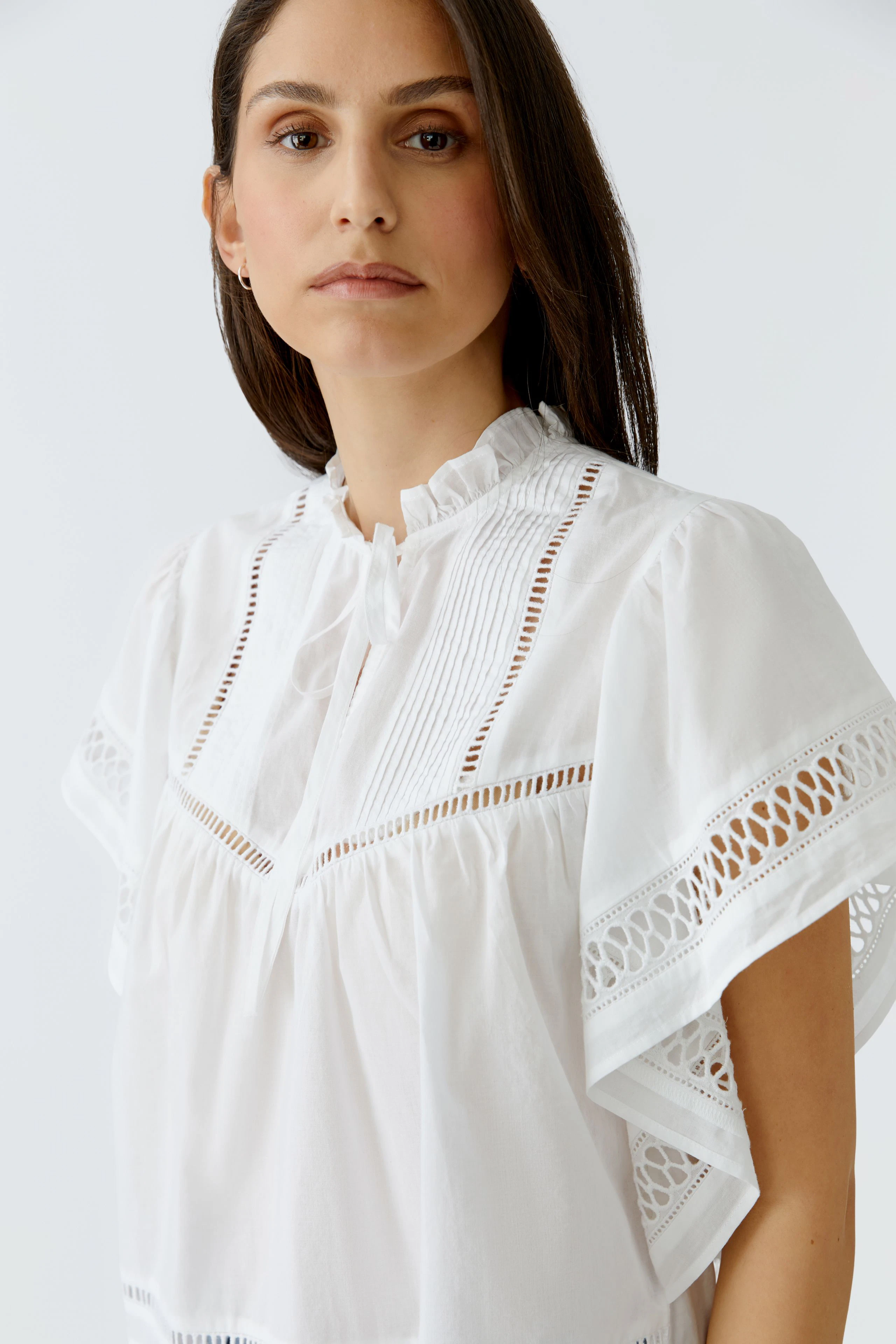 White blouse: Woman in a white blouse with lace details and a relaxed fit, looking confidently.