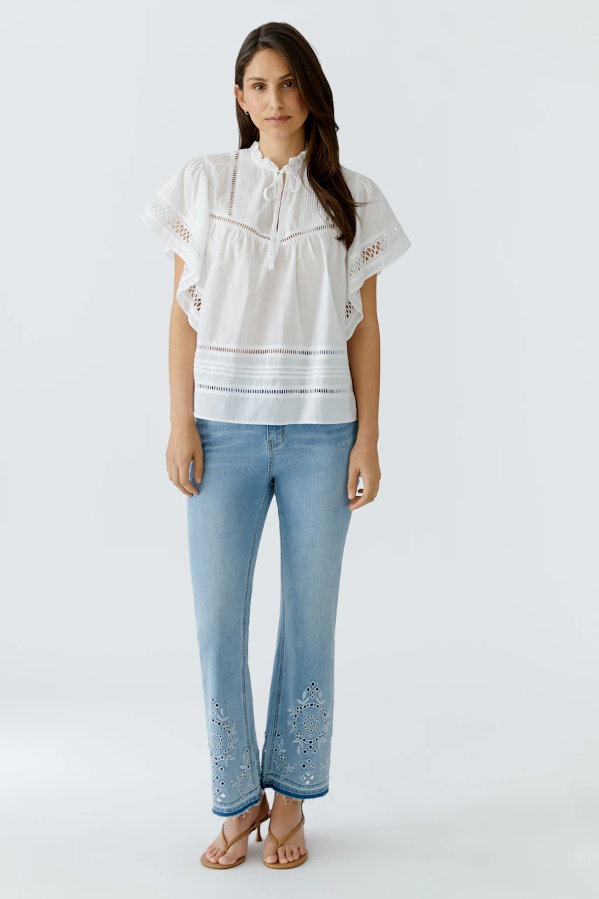 Weiße Damen-Bluse: Frau in lockerer Bluse mit Spitzen-Details und Jeans, lässig und modern.
