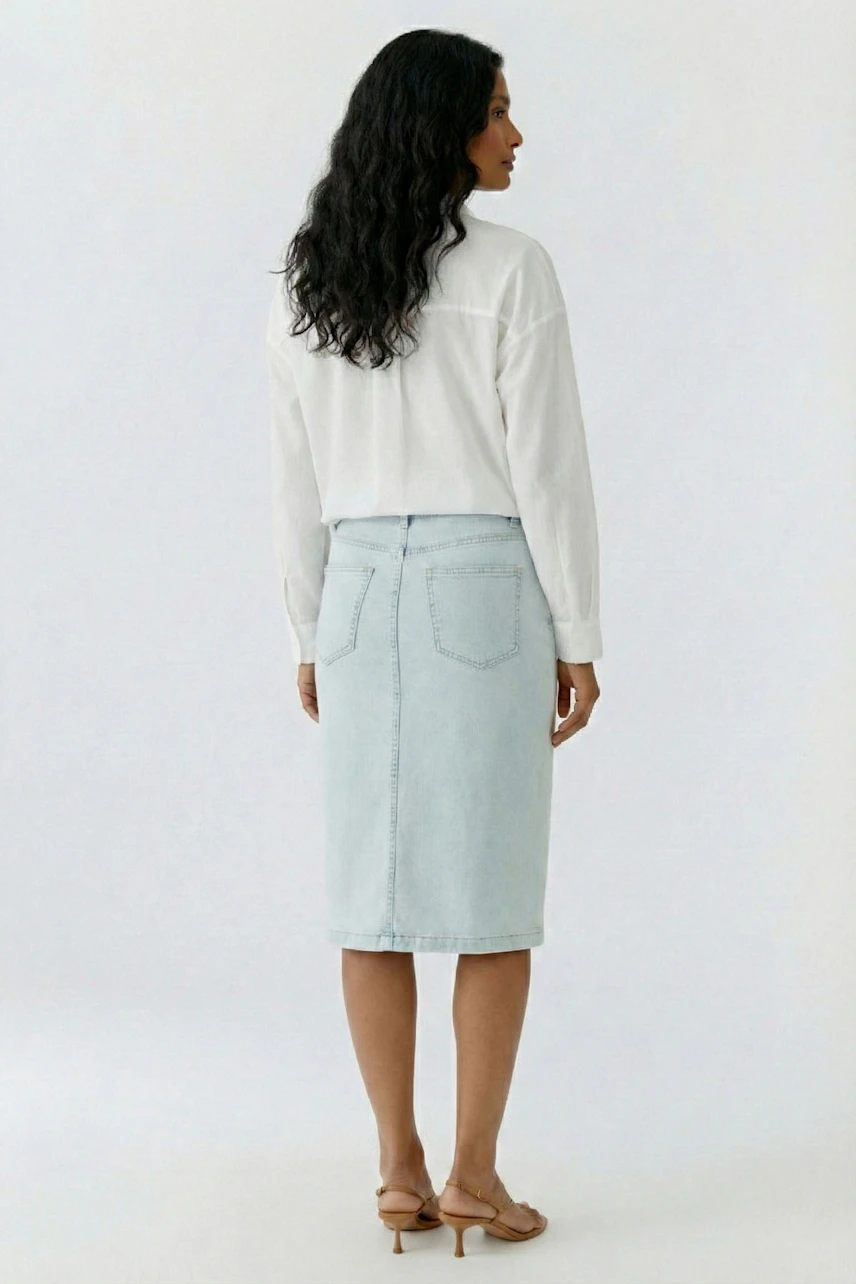 Casual women's shirt blouse: Woman in white blouse and light denim skirt, standing with back view.
