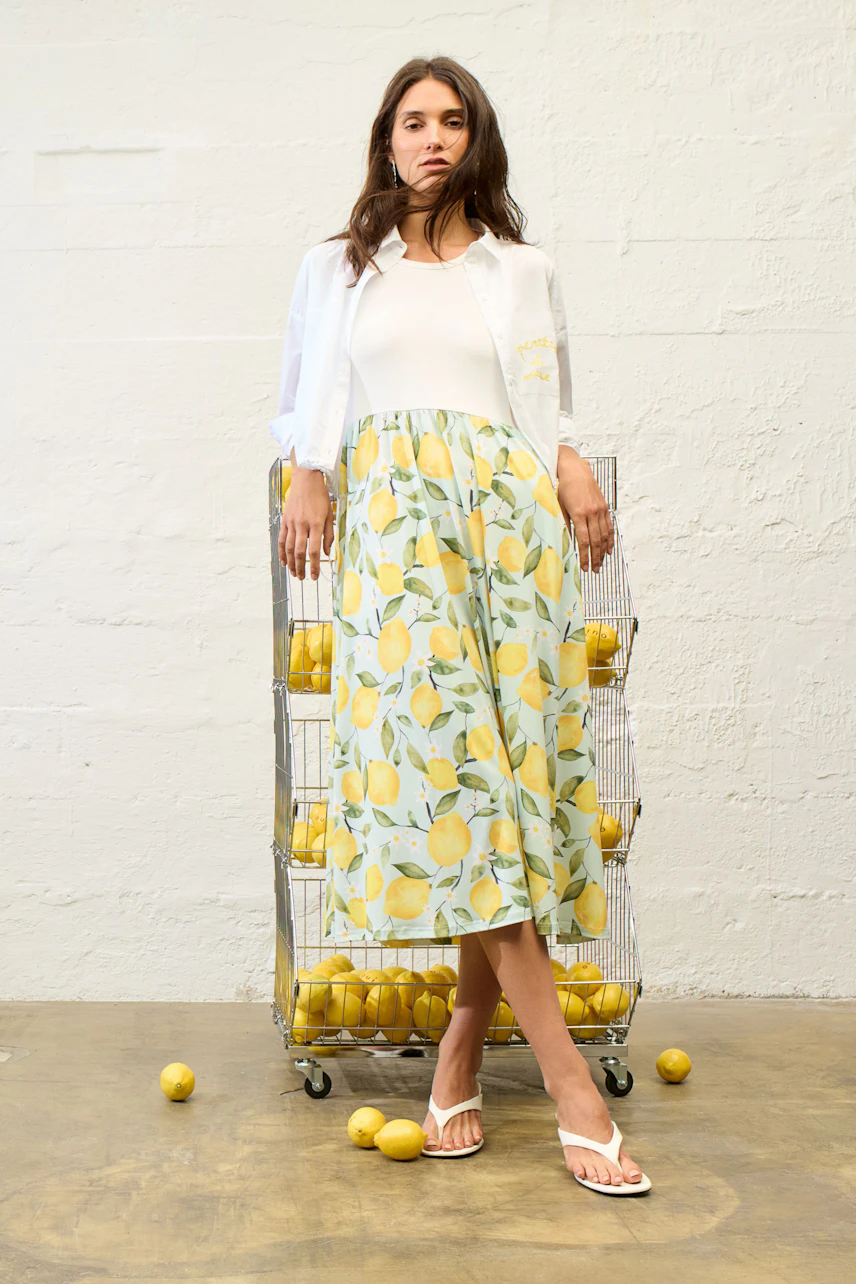 Casual women's shirt blouse: Woman in a white blouse over a lemon-patterned dress, standing confidently.