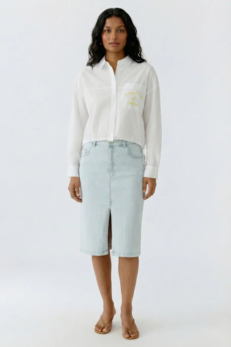 White shirt blouse with yellow text on pocket, featuring a classic collar and button-up front.