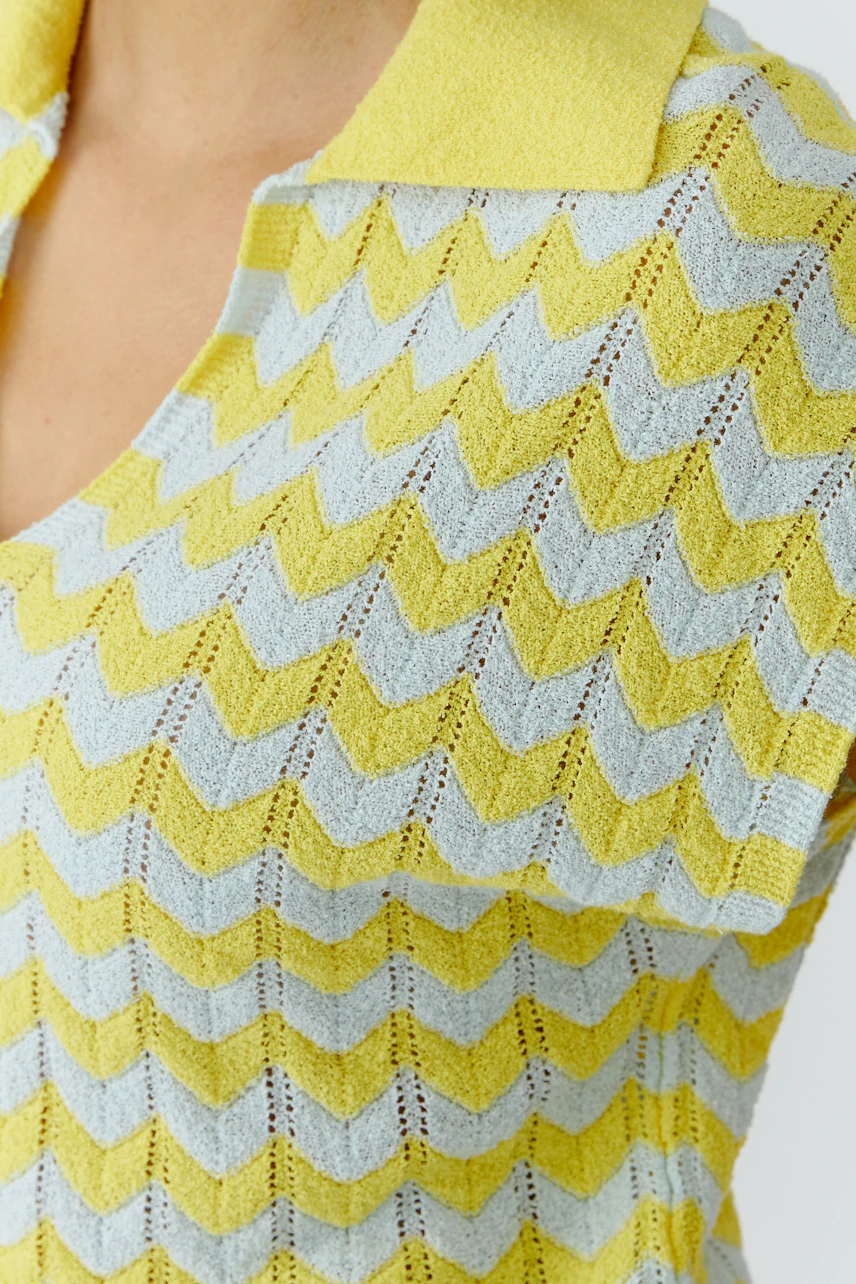 Frau im gelb-blauen Pullover mit Zickzack-Muster und Kragen, frischer Look.