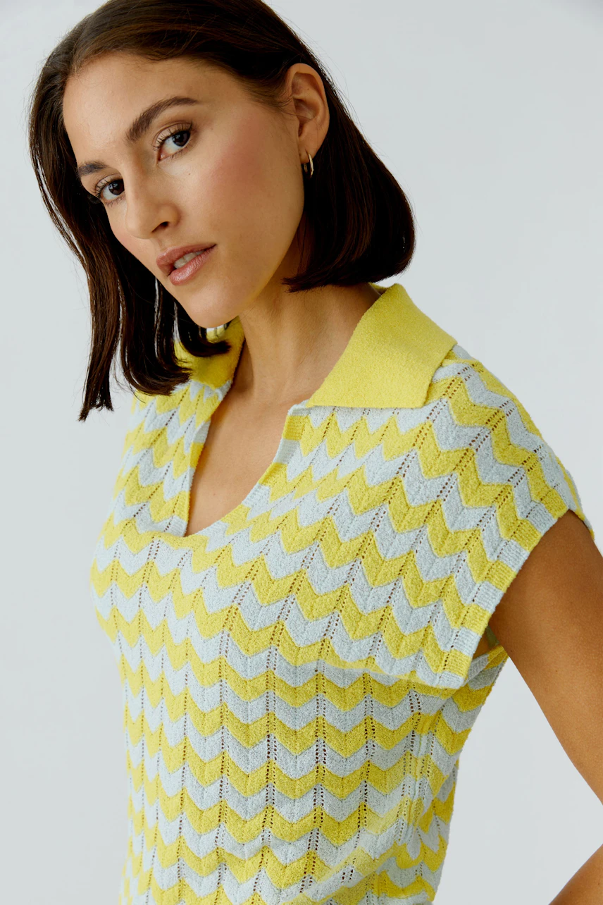Frau im gelb-weißen Pullover mit Zickzackmuster und Kragen, lässiger Look.