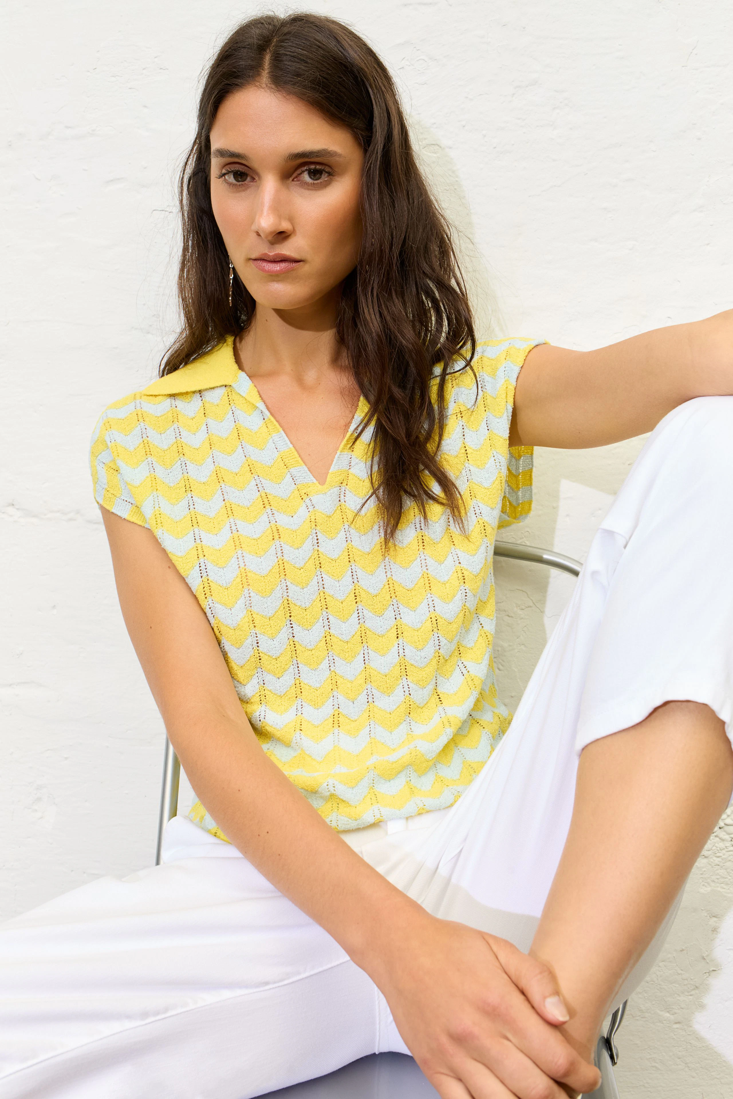 Casual women's pullover: Woman in a yellow zigzag pullover with white pants, sitting relaxed.