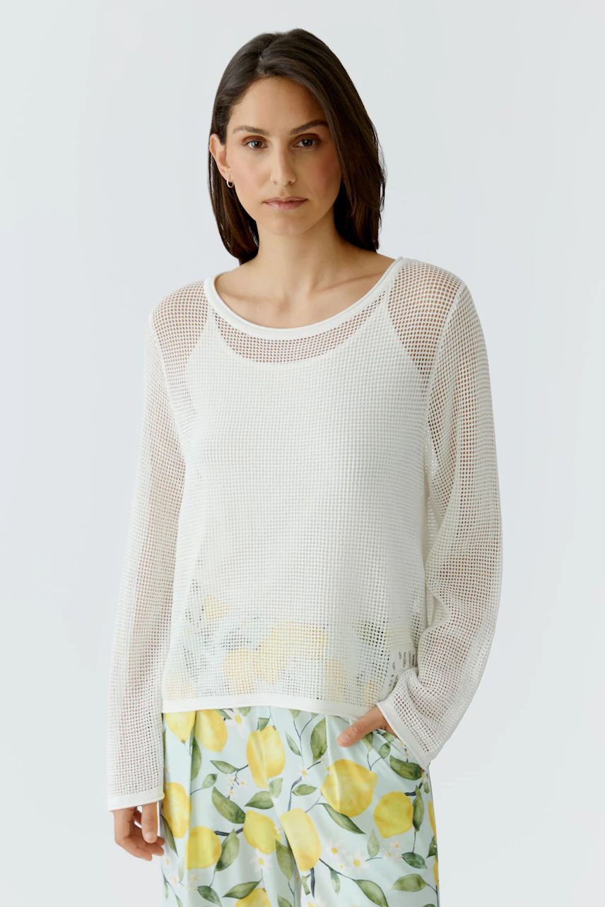 Lässiger Damen-Pullover: Frau im weißen Netzpullover mit Zitronenprint-Hose, entspannt und modern.