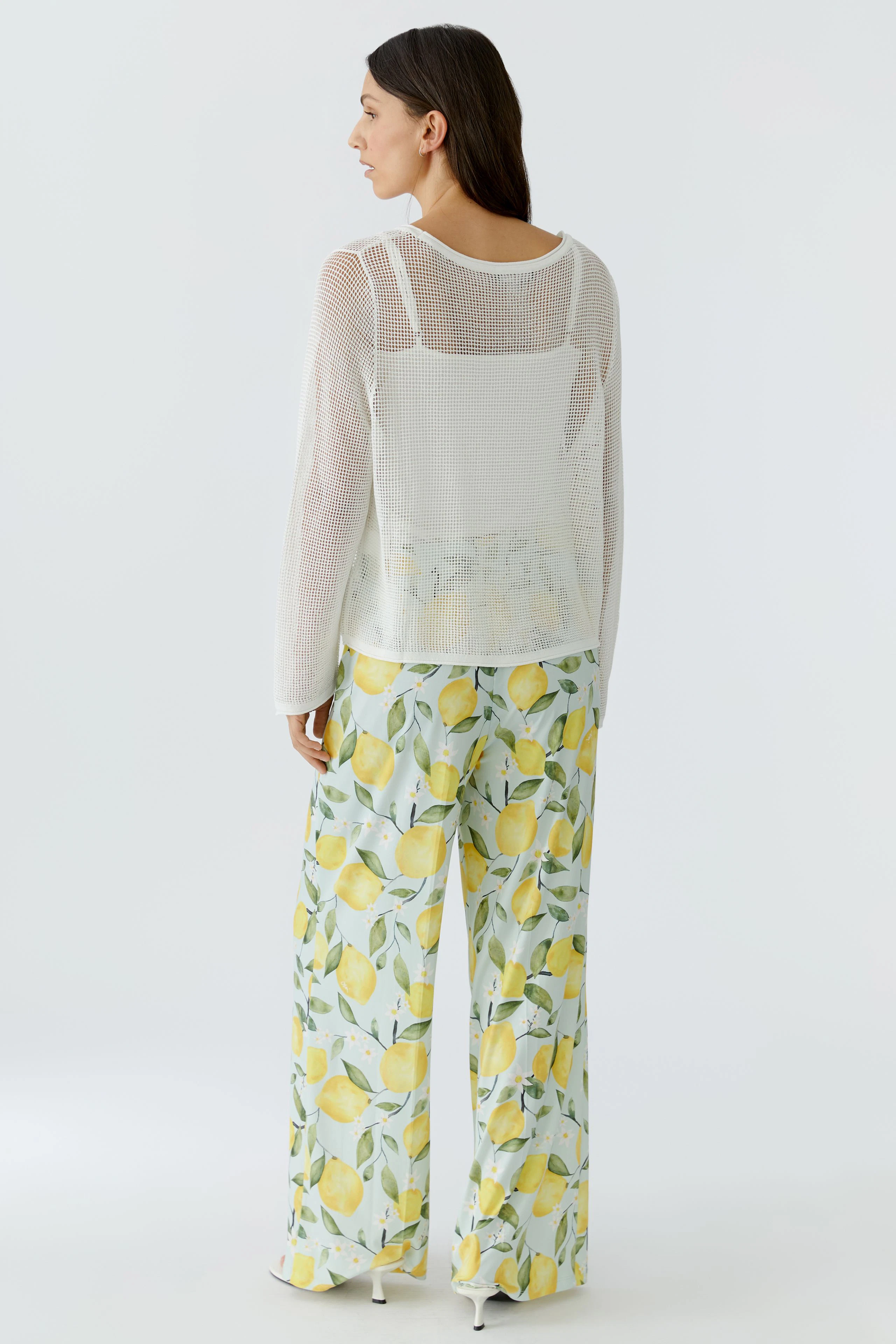 Lässiger Damen-Pullover: Frau im weißen Pullover mit transparentem Design und sommerlicher Hose mit Zitronenmuster.