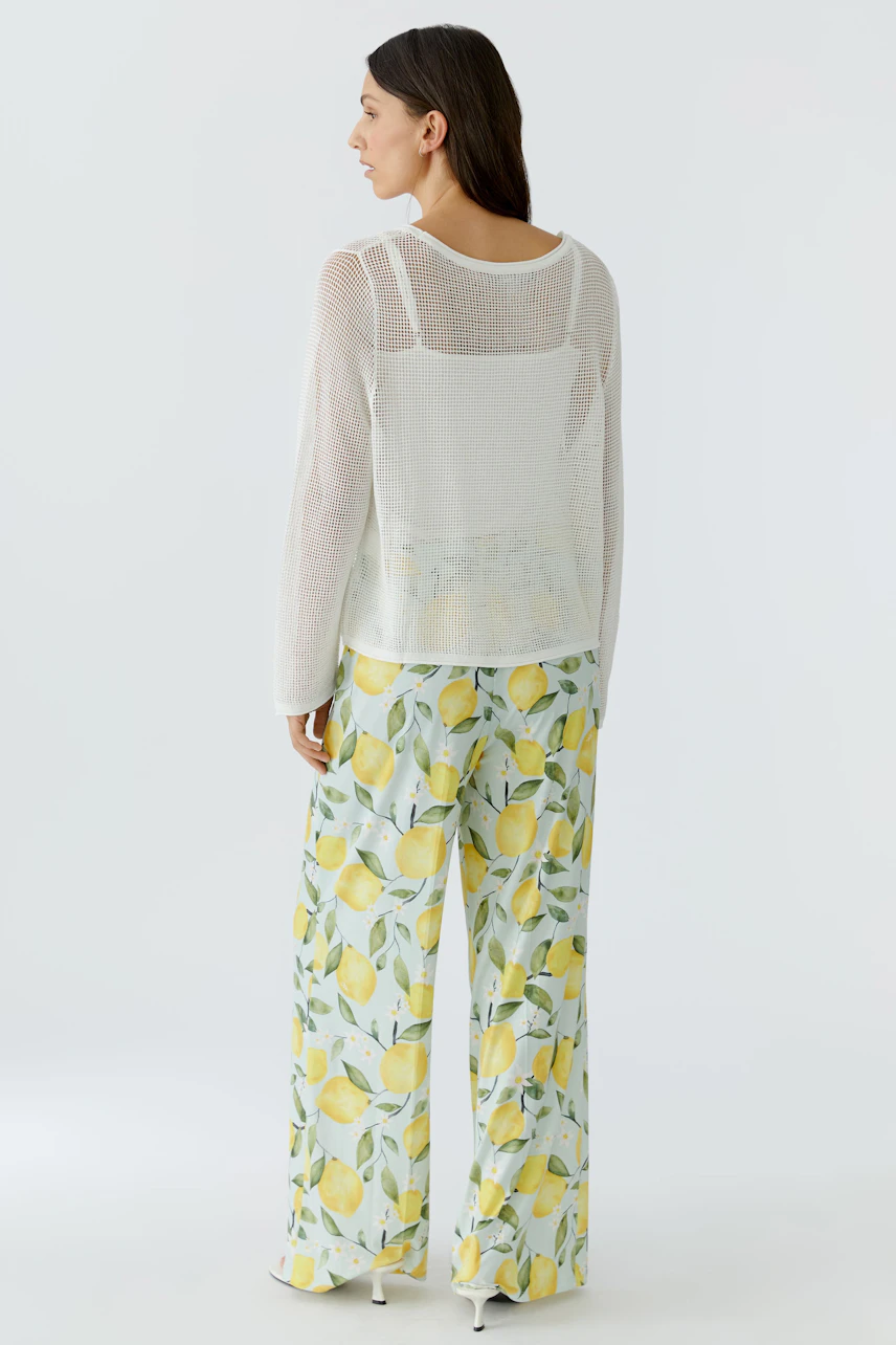 Lässiger Damen-Pullover: Frau im weißen Pullover mit transparentem Design und sommerlicher Hose mit Zitronenmuster.