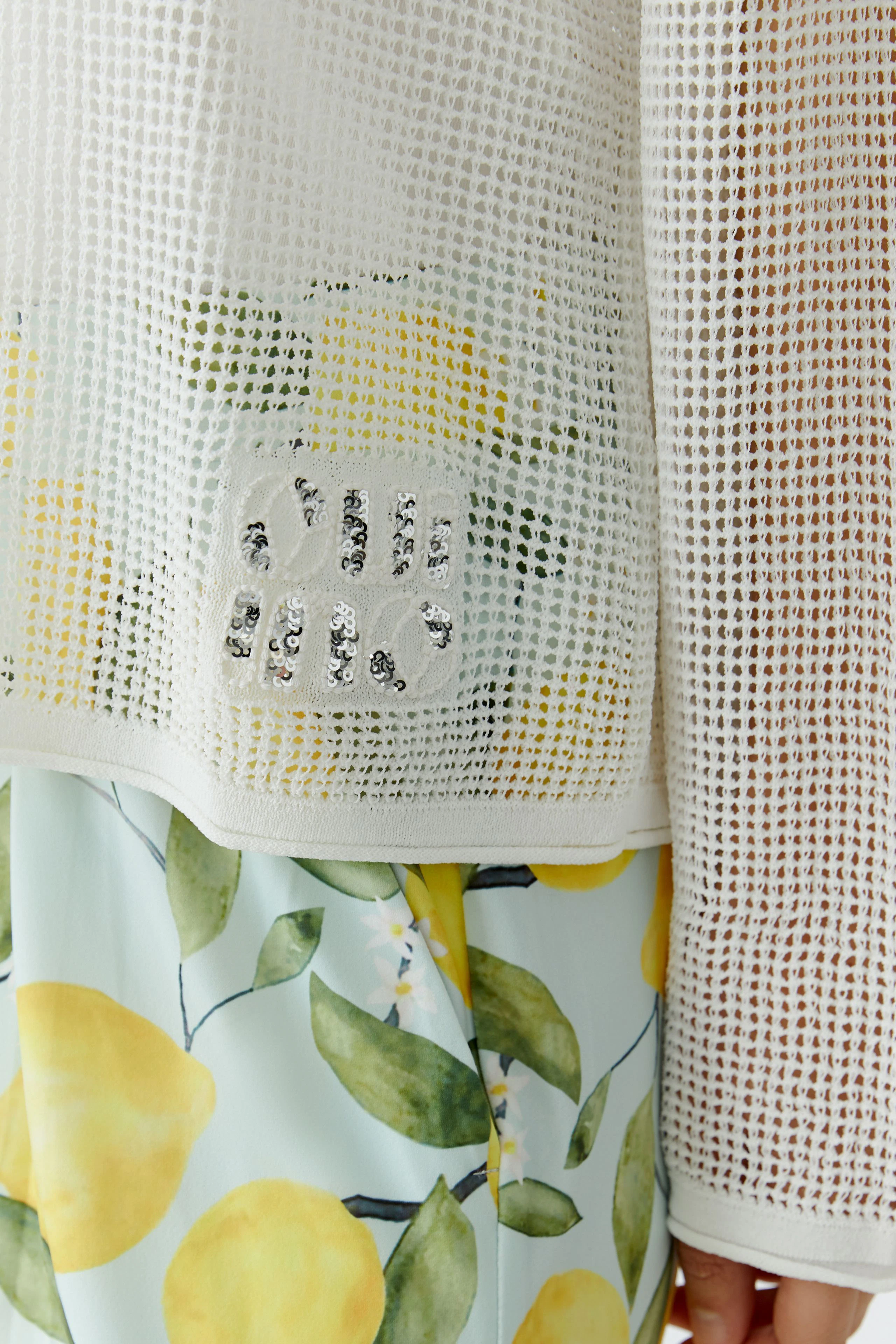 Damen-Pullover: Weißer Netzpullover mit funkelndem Detail, kombiniert mit Zitronenprint-Rock.